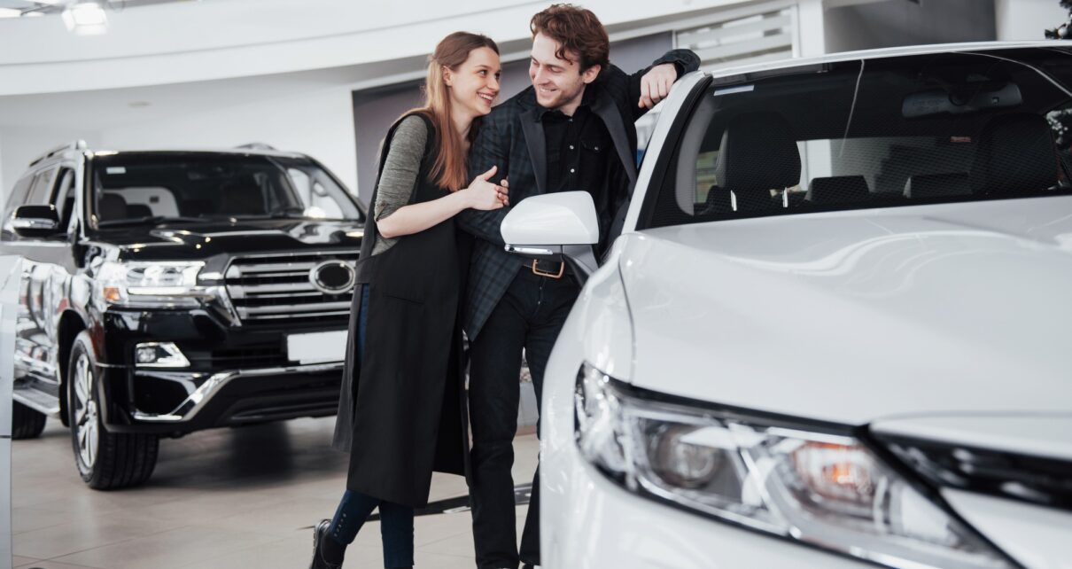 I like this car. Beautiful young couple standing at the dealership choosing the car to buy