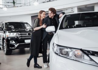 I like this car. Beautiful young couple standing at the dealership choosing the car to buy
