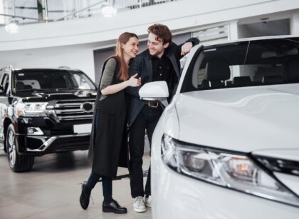 I like this car. Beautiful young couple standing at the dealership choosing the car to buy