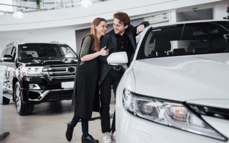 I like this car. Beautiful young couple standing at the dealership choosing the car to buy