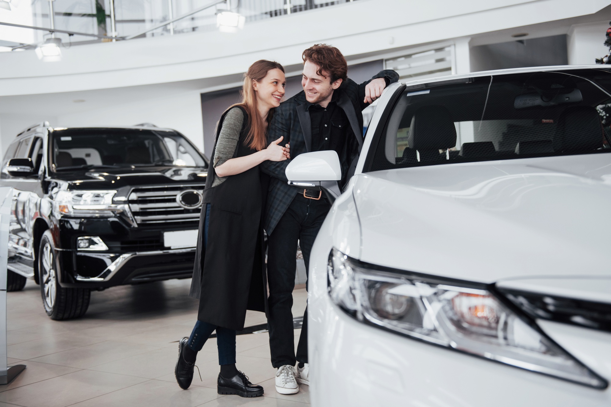 I like this car. Beautiful young couple standing at the dealership choosing the car to buy