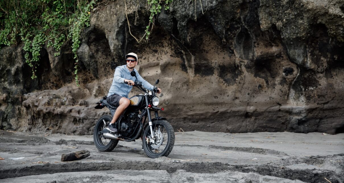 Man in cap riding motorcycle on beach. Moto cross dirtbiker on beach sunset on Bali. Young hipster