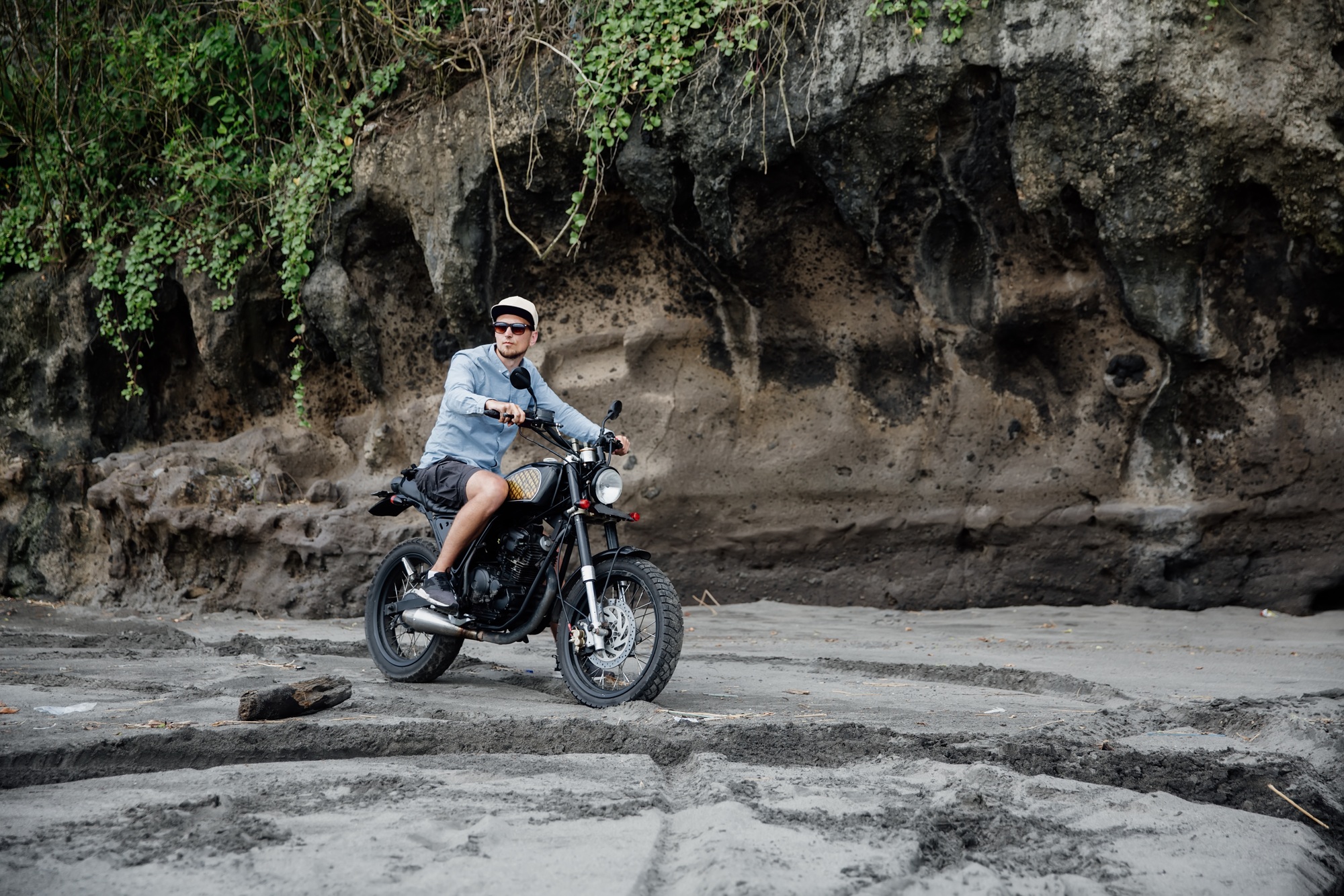 Man in cap riding motorcycle on beach. Moto cross dirtbiker on beach sunset on Bali. Young hipster