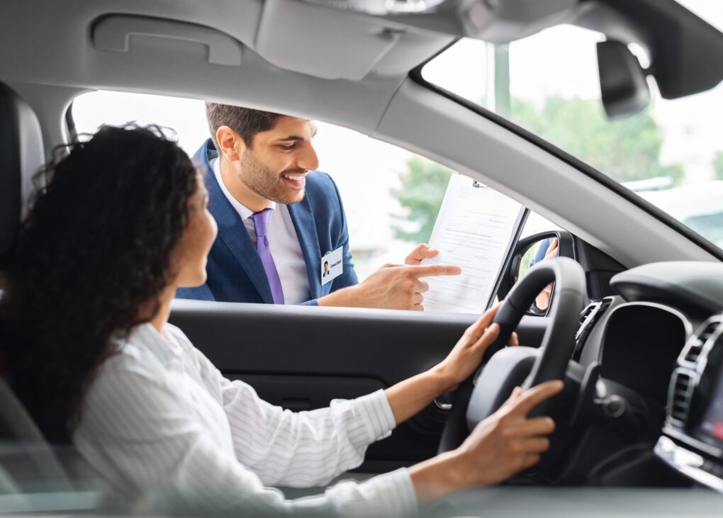 Young woman sitting inside car, having conversation with sales manager