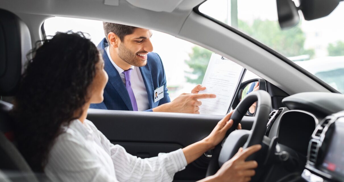 Young woman sitting inside car, having conversation with sales manager