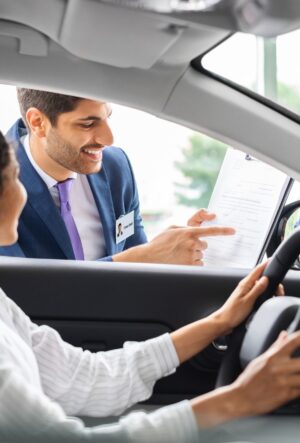 Young woman sitting inside car, having conversation with sales manager