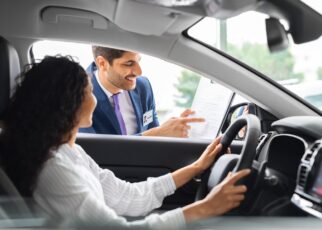 Young woman sitting inside car, having conversation with sales manager