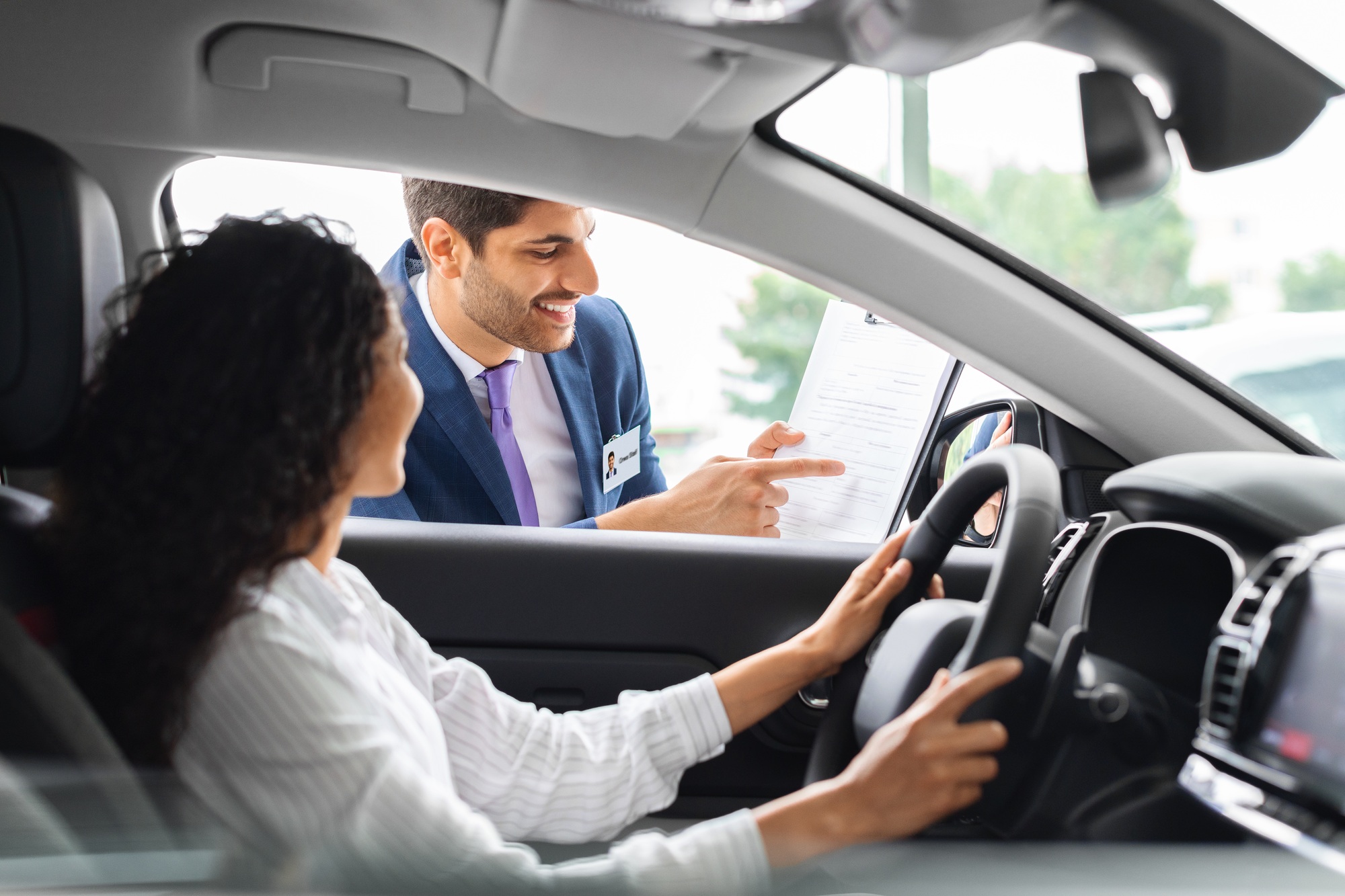 Young woman sitting inside car, having conversation with sales manager